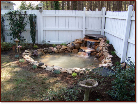 Pond with waterfall in corner of white board fence